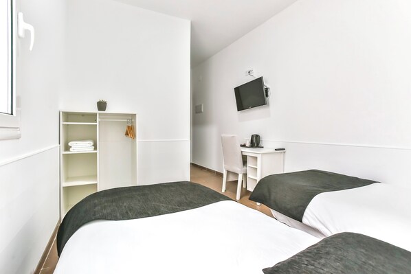 A hotel room with two beds, a desk, a chair, a TV, and a wardrobe. - Laramond Barcelona Rooms (Barcelona)
