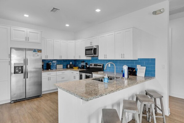 Una cocina moderna con armarios blancos, un refrigerador de acero inoxidable, un microondas y una encimera de granito.