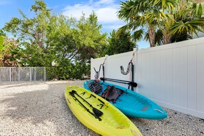 Two kayaks with paddles and life jackets, a white fence, and a gravel ground.