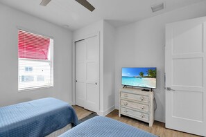 Un dormitorio con dos camas, un televisor sobre una cómoda y una ventana con persianas.