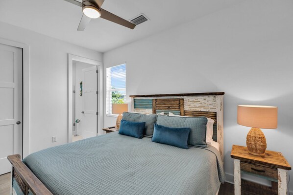 Un dormitorio con cama, mesita de noche, lámpara, ventilador de techo y ventana con persianas.