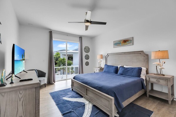 A bedroom with a bed, bedside tables, a desk, a television, and a balcony with a view.