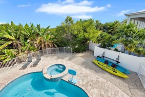 A swimming pool with a hot tub, surrounded by a white fence, and a kayak docked against the wall.