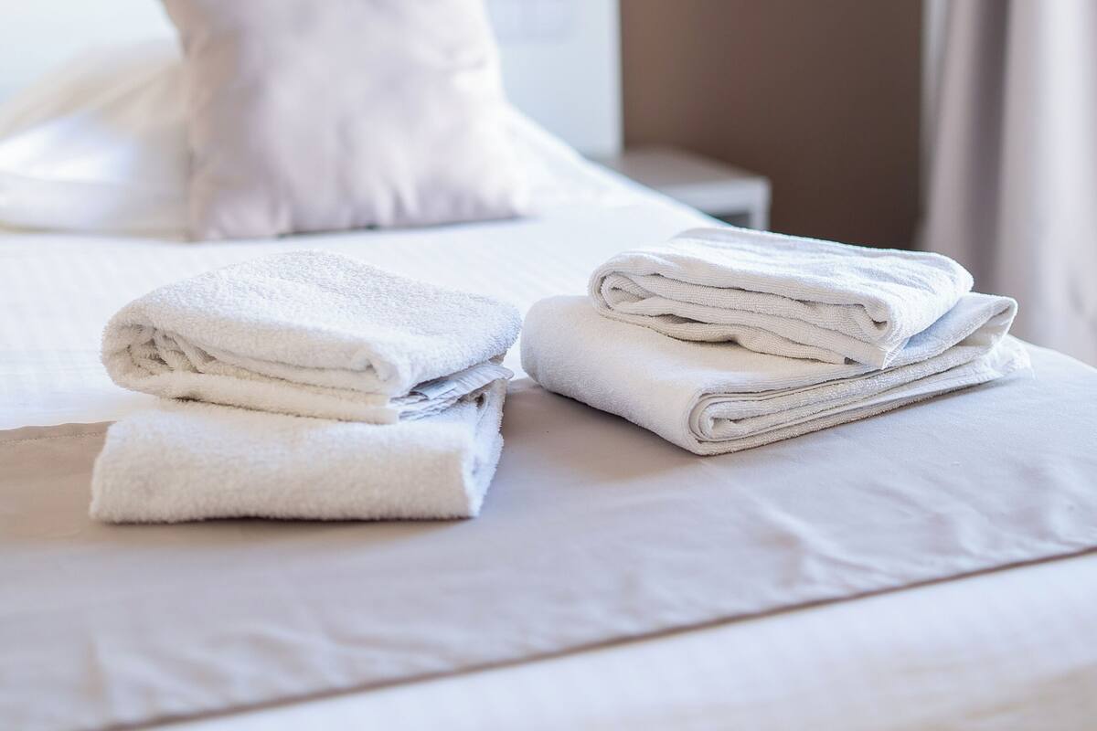 Una cama bien hecha con toallas blancas dobladas, una almohada blanca y un teléfono junto a la cama.