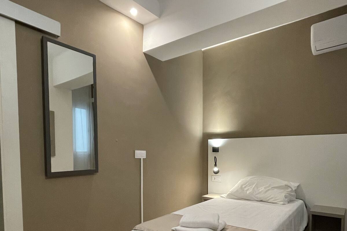 Un dormitorio con una cama, una mesita de noche, una lámpara de pared y un espejo.