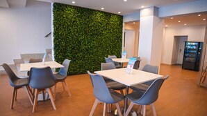 Un espacio interior moderno con mesas, sillas, una pared verde y una máquina expendedora.