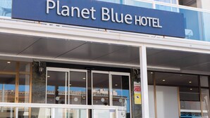 Exterior del Hotel Planet Blue, con un letrero visible, una entrada de vidrio y una escalera que conduce a la entrada.