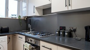 Una cocina moderna con estufa a gas, horno y lavavajillas integrado. Hay tres recipientes negros etiquetados como “té”, “café” y “café”.