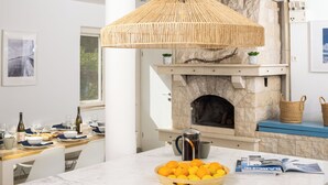 A kitchen with a stone fireplace, a wicker hanging light fixture, and a bowl of oranges on the counter.