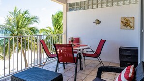 A balcony with a table and chairs, a small cabinet, and a decorative wall piece.