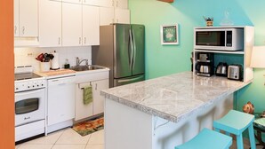 A modern kitchen with white cabinets, a stainless steel refrigerator, a microwave, a coffee maker, and a toaster.