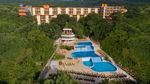 Resort com várias piscinas, uma torre central e uma área verde e arborizada.