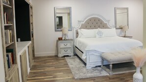 A bedroom with a large bed, two bedside tables, a nightstand, a bookshelf, and a mirror. - Romantic Private Space for Couple's Getaway w/Hot Tub (Buena Vista)
