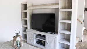 A living room with a TV on a white entertainment unit, a small table with a lantern, and a staircase to the right. - Romantic Private Space for Couple's Getaway w/Hot Tub (Buena Vista)
