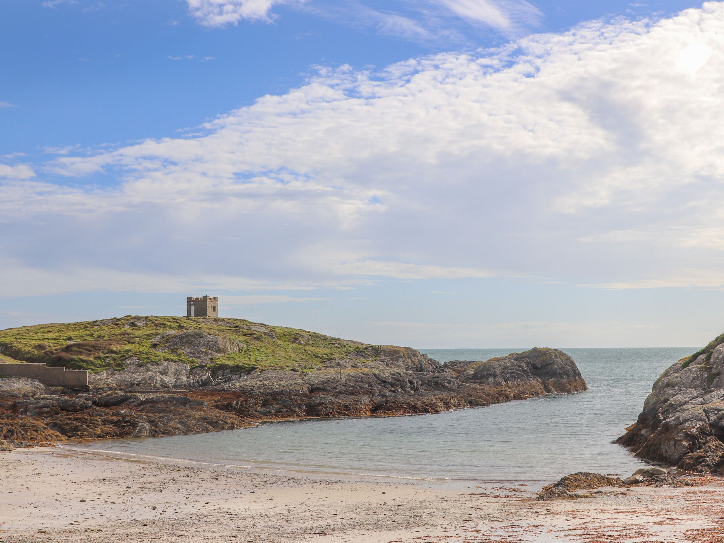 Un paysage côtier avec un château perché sur une colline, une côte rocheuse et une mer calme.