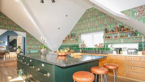 A kitchen with a green island, bar stools, and a view of the living area. - Glan Towyn (Holyhead)