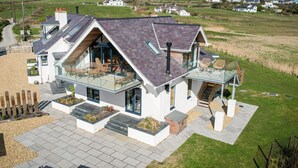 A modern house with a large glass balcony, a spacious patio, and a view of the surrounding countryside. - Glan Towyn (Holyhead)