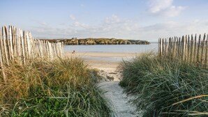 A sandy beach path leading to a calm sea, flanked by wooden fences and grassy vegetation. - Glan Towyn (Holyhead)