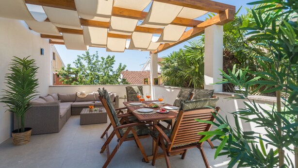 Un patio al aire libre con una mesa y sillas de madera, un sofá y una planta en maceta.