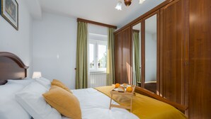 Un dormitorio con cama, un armario de madera, un ventanal con cortinas y una bandeja con naranjas y pan.
