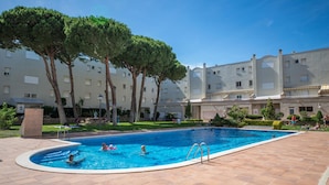 Une piscine entourée d’une cour plantée d’arbres, avec un immeuble à plusieurs étages en arrière-plan.