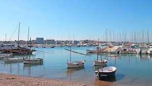 Un port de plaisance où sont amarrés différents types de bateaux, un ciel dégagé et une vue lointaine sur la ville.