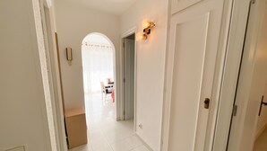 Un couloir aux murs blancs, doté d’un sol carrelé et d’une porte avec un luminaire.
