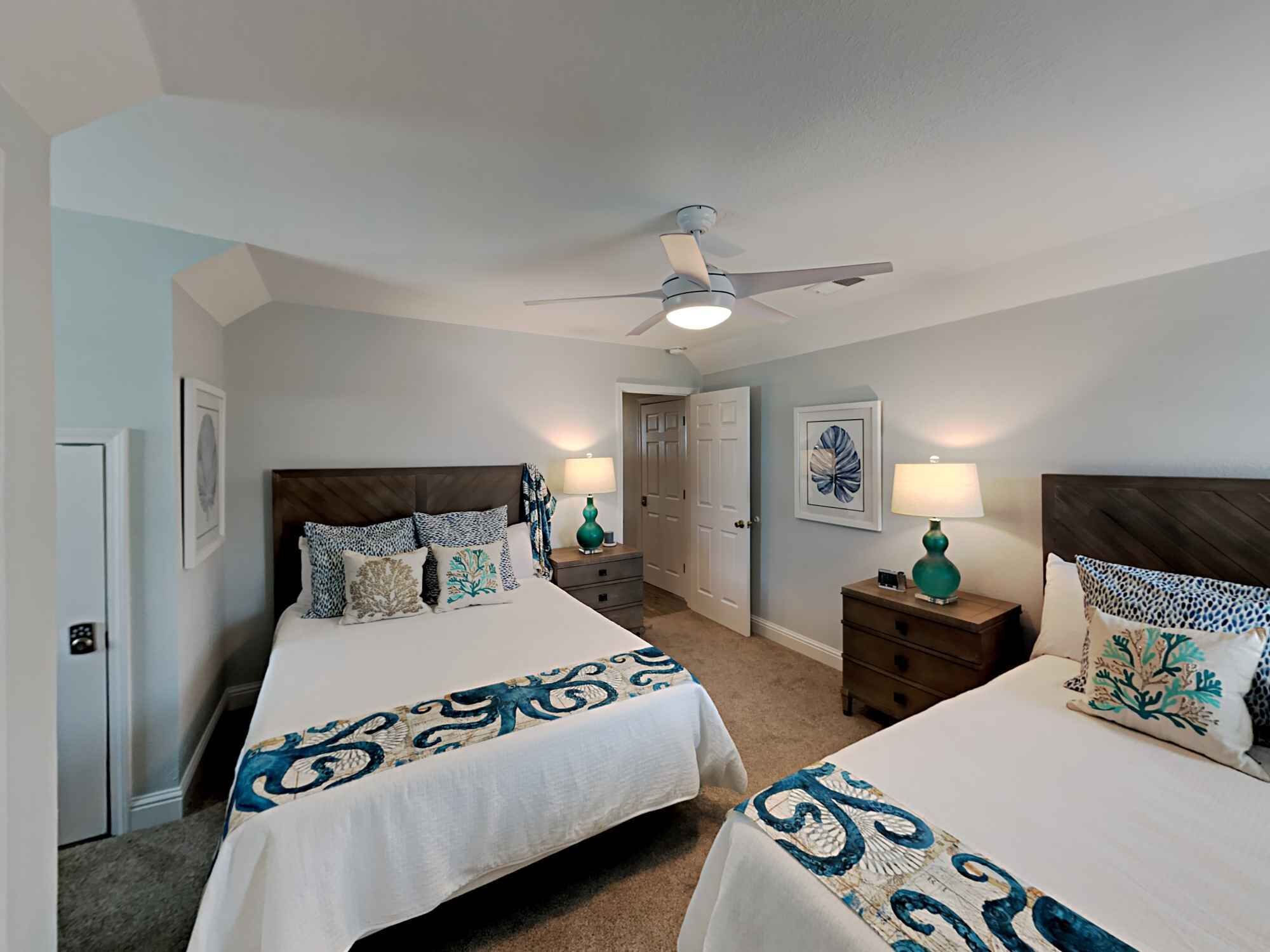 A bedroom with two beds, a ceiling fan, and a door leading to another room.