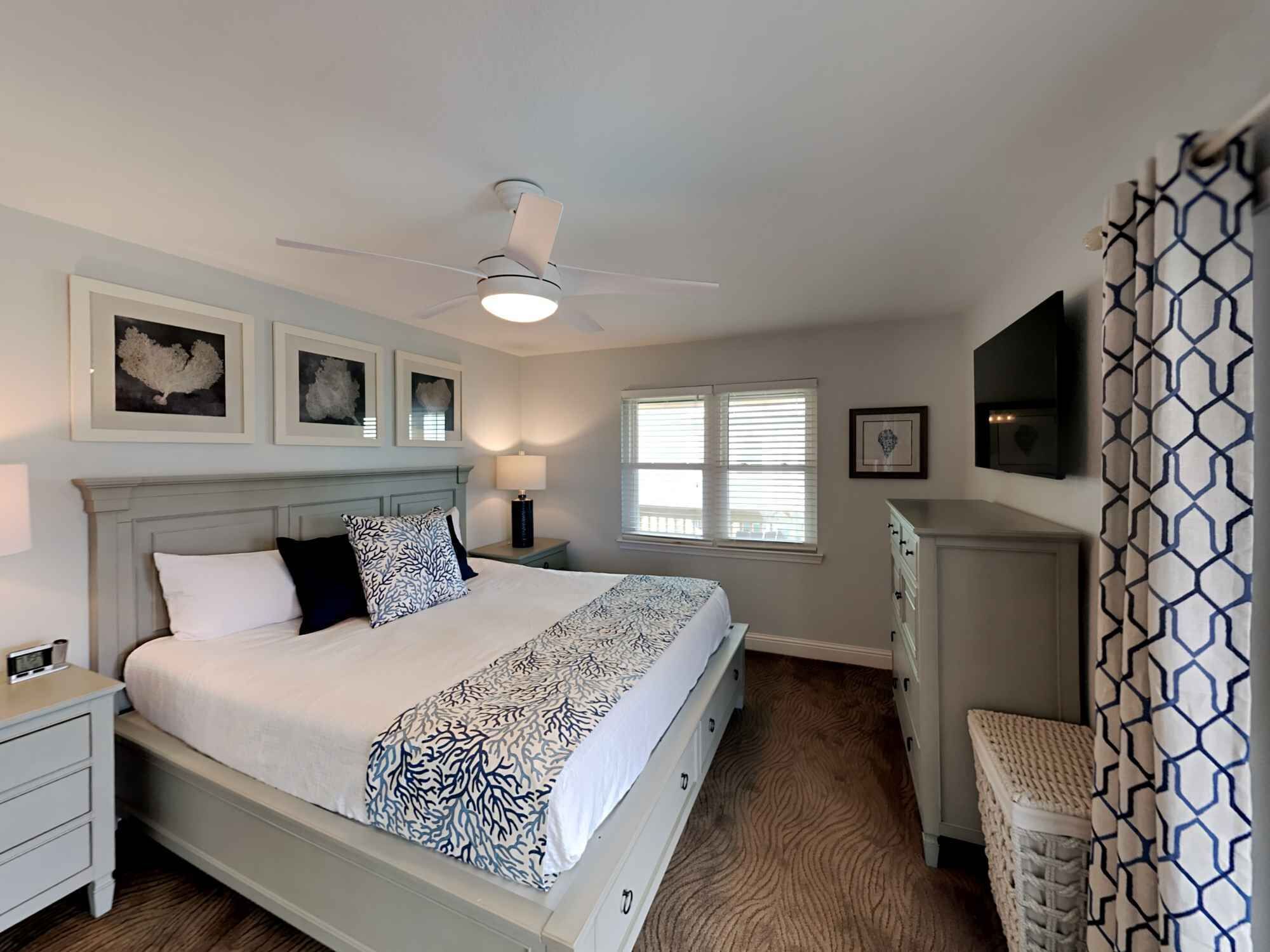 A bedroom with a bed, nightstands, a dresser, a ceiling fan, and a window with blinds.