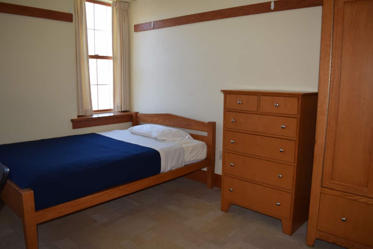 Une chambre avec un lit simple, une commode en bois et une fenêtre avec des rideaux.