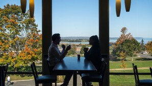 A couple dining at a table with a view of a river and buildings in the background. - Acadia University (Wolfville)