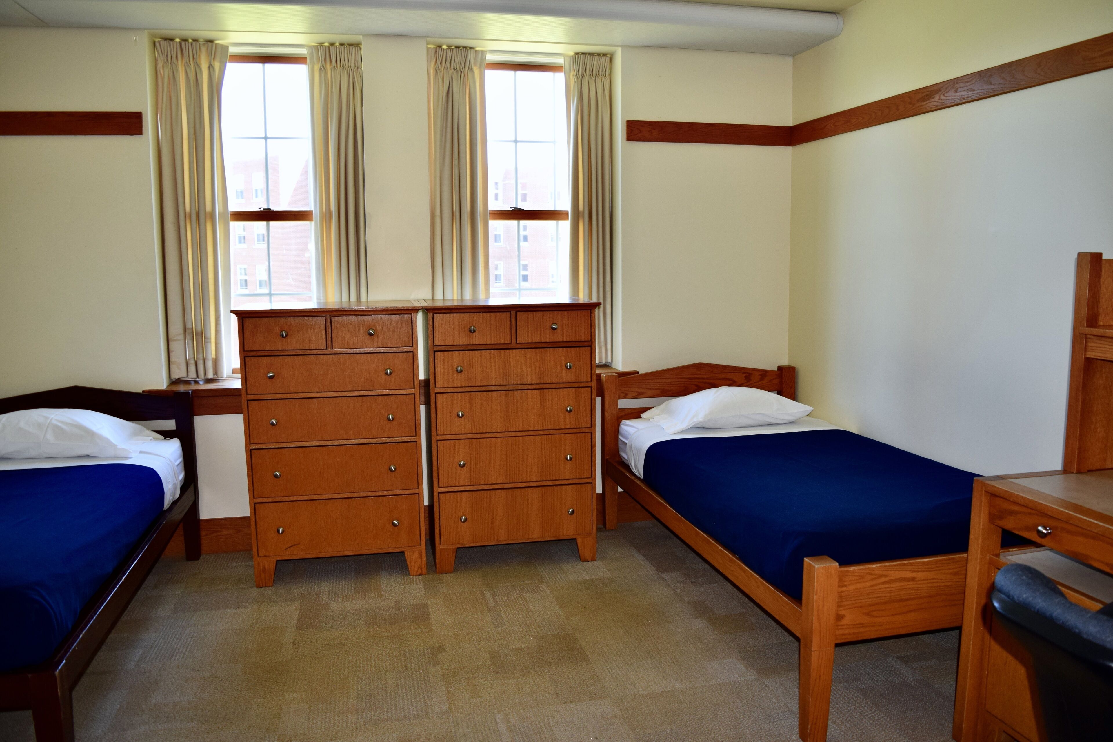 A room with two wooden beds, a wooden dresser, and a desk.