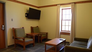 A room with a flat-screen TV mounted on the wall, two wooden chairs with cushions, a wooden table, and a sofa. - Acadia University (Wolfville)