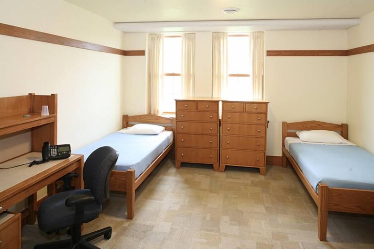 Une chambre avec deux lits simples, une commode en bois, un bureau avec une chaise et un téléphone.