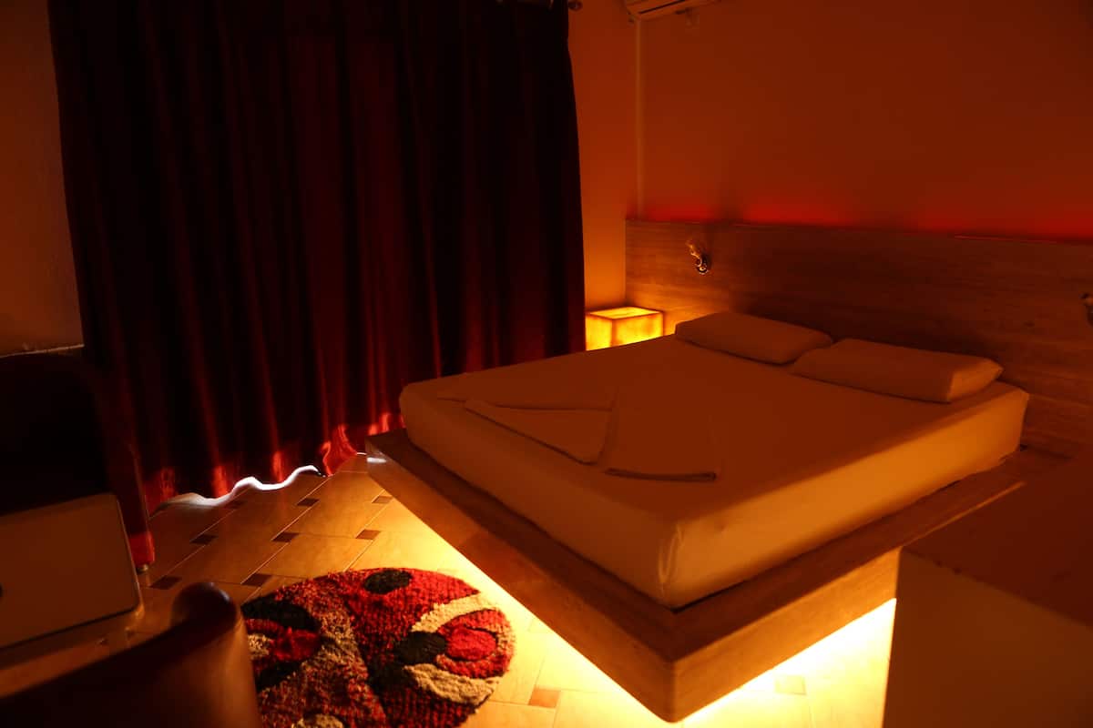 A bedroom with a bed, a nightstand, a lamp, and a red curtain.