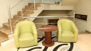 Una habitación con una escalera, dos sillones verdes, una mesa redonda de madera y una alfombra estampada.