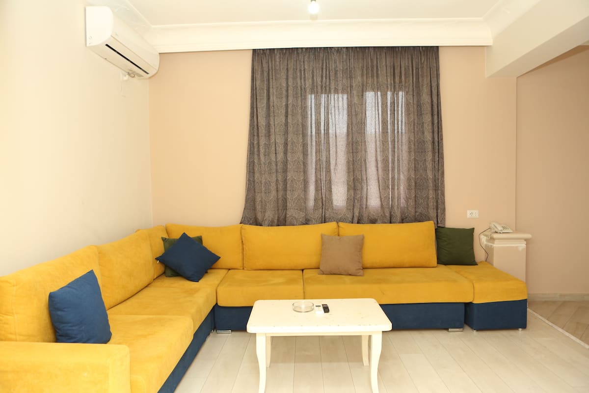 A living room with a yellow sofa, a white coffee table, and a grey curtain.