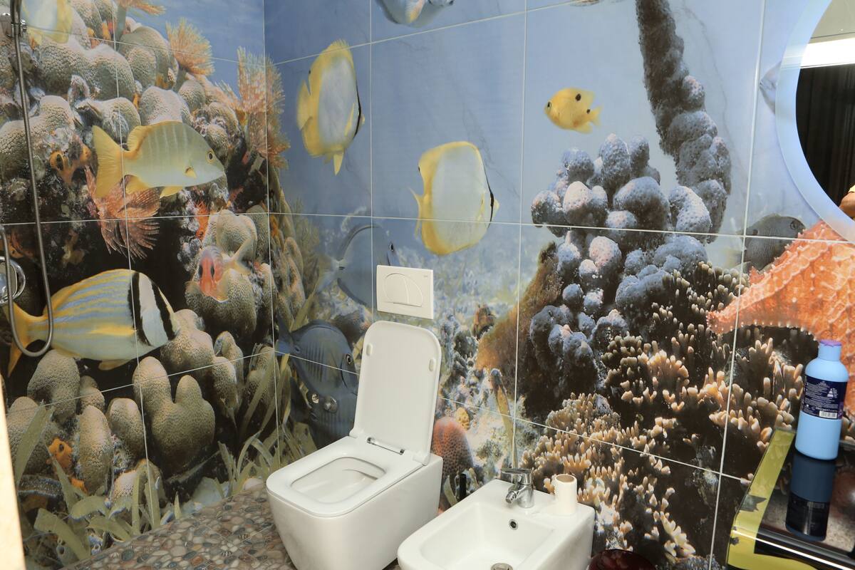 A bathroom with a toilet and sink, surrounded by a mural of an underwater scene.