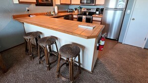 A kitchen with a central island, bar stools, a microwave, a refrigerator, and a fire extinguisher. - SBC #106 Oceanfront - Hear the Ocean, Steps to the Promenade and Beach Access (Seaside)