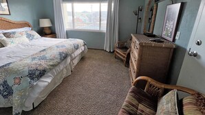 A bedroom with a bed, a dresser, a chair, a window with curtains, and a television. - SBC #106 Oceanfront - Hear the Ocean, Steps to the Promenade and Beach Access (Seaside)