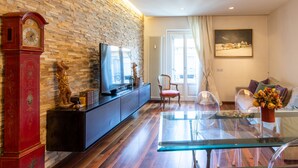 A living room with a brick wall, a red clock, a TV, a glass table, a sofa, and a painting. - Porta Venezia-Design apartment, 2-bedrooms, Netflix, wifi (Milano)