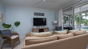 A living room with a beige sofa, a wicker chair, a flat-screen TV, and a 'Beach House' sign on the wall. - Nice and cozy home is just a short walk to the beach and pool! (Key Colony Beach)
