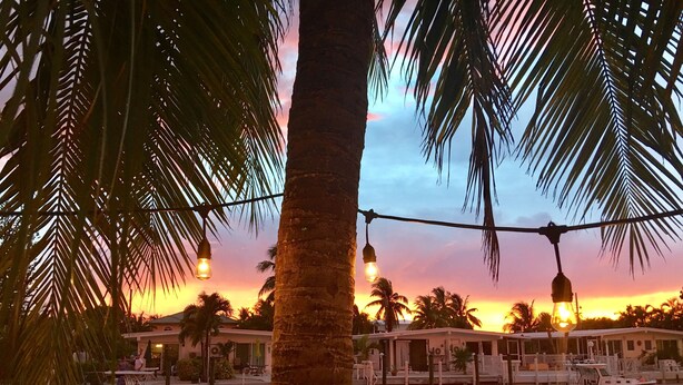 A waterfront hotel with boats docked, palm trees, and string lights. - Nice and cozy home is just a short walk to the beach and pool! (Key Colony Beach)