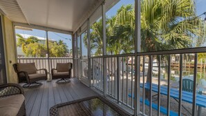 A covered outdoor area with wicker furniture, a glass table, and a view of palm trees and a pool. - Nice and cozy home is just a short walk to the beach and pool! (Key Colony Beach)