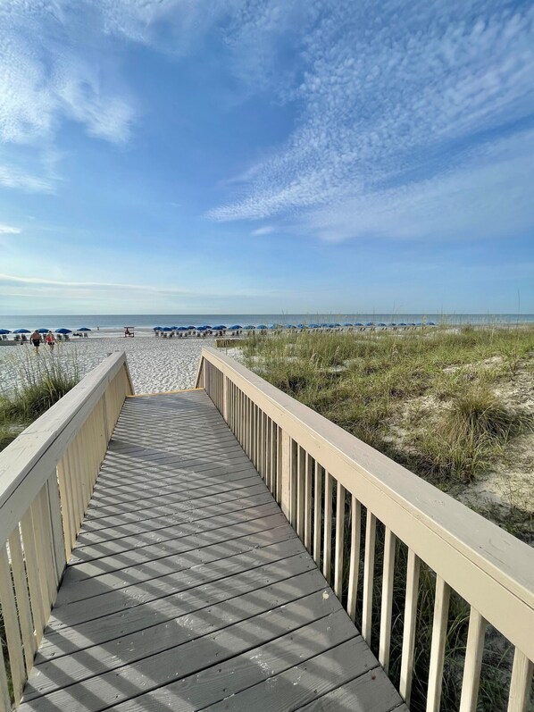 En træpromenade der fører til en strand med parasoller og sand.