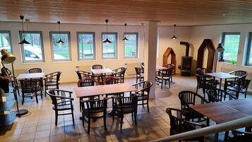 A spacious indoor dining area with multiple tables and chairs, large windows, and a wooden ceiling.