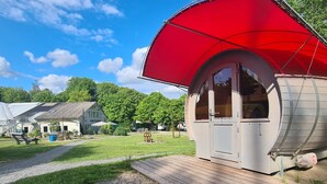 A small, single-story building with a red awning, a wooden deck, and a grassy area with a path leading to it. - Haus der Schmetterlinge (Uslar)