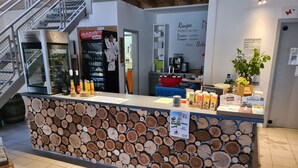 A reception desk with a wood log wall, a staircase, and a menu board. - Haus der Schmetterlinge (Uslar)