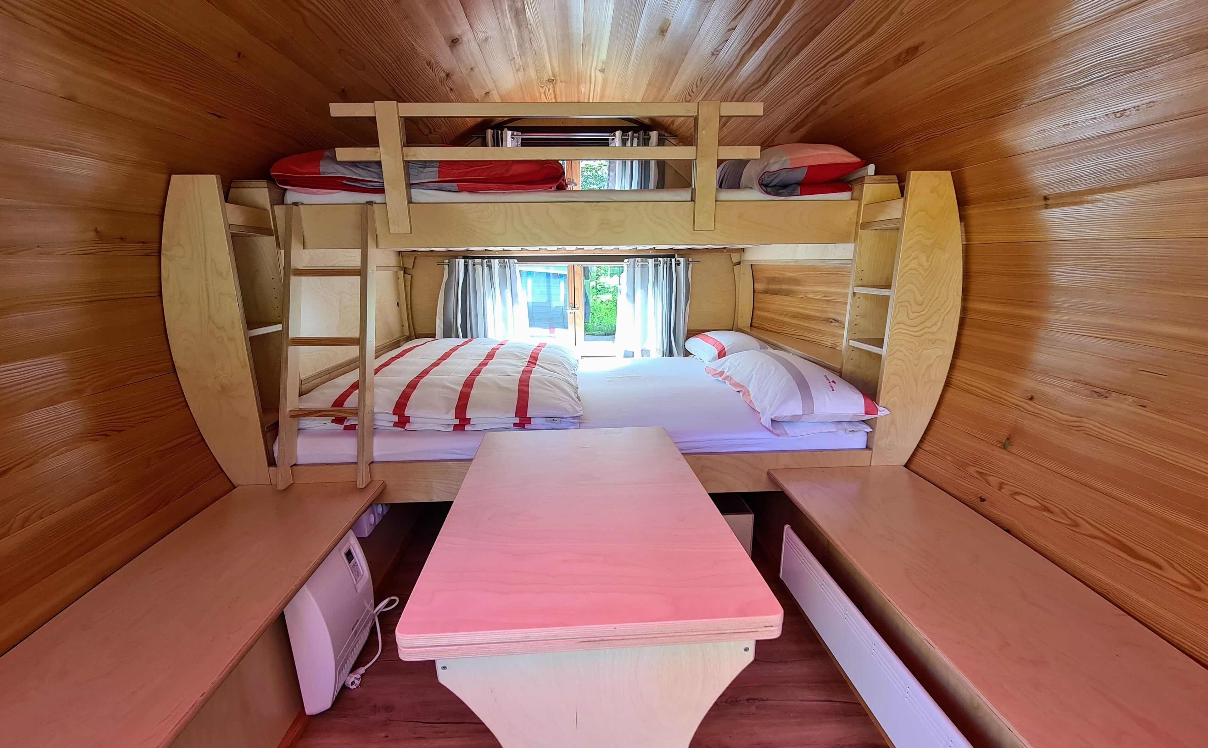 A bunk bed room with a wooden interior, a desk, and a window with curtains.