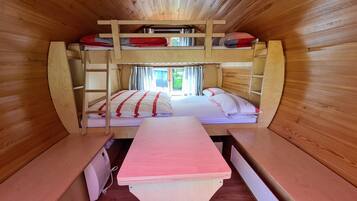 A bunk bed room with a wooden interior, a desk, and a window with curtains.